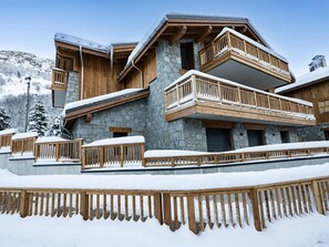 Una cabaña de varios pisos con paredes de piedra, balcones de madera y un techo cubierto de nieve.