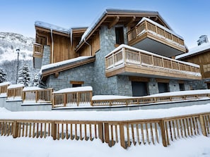 Una cabaña de varios pisos con paredes de piedra, balcones de madera y un techo cubierto de nieve.