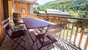 A wooden balcony with a table and chairs, overlooking a mountainous landscape.