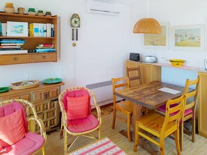 A cozy dining area with a wooden table, wicker chairs, and a bookshelf with books and decorative items.