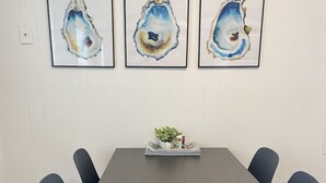 A dining table with six chairs, three framed artworks on the wall, and a small plant on the table.
