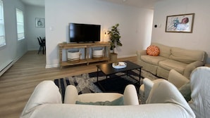 A living room with a television, sofa, and coffee table. There is a plant and a painting on the wall.