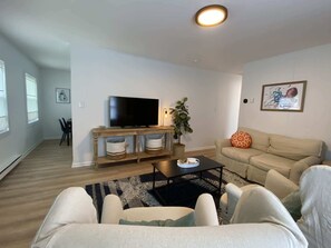 A living room with a television, sofa, and coffee table. There is a plant and a painting on the wall. - Cozy Oaks Home Near Park, Pickleball & Beach (Cape Charles)