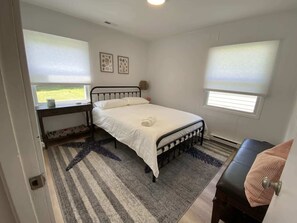 A bedroom with a single bed, a desk, and two windows with blinds.