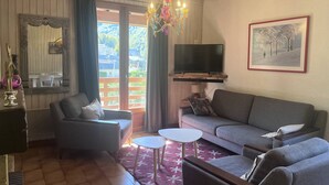 A living room with a sofa, armchairs, a TV, a chandelier, and a large window with curtains.
