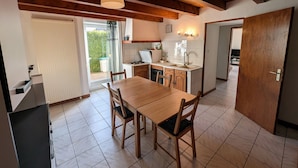 A compact kitchen with a dining area, wooden ceiling beams, and a view through the window.
