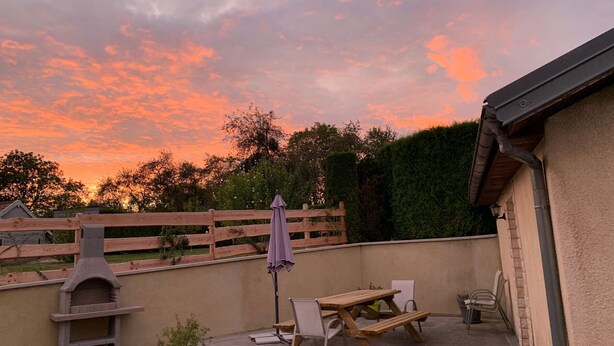 An outdoor patio area with a wooden table and chairs, a barbecue grill, and potted plants.