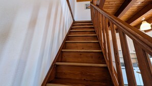 A wooden staircase with a handrail, white walls, and a wooden ceiling.
