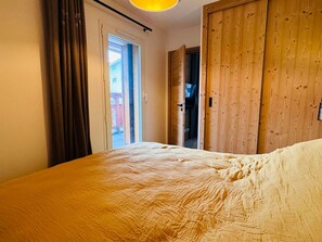 A bedroom with a bed, a wooden wardrobe, and a door leading to a balcony.