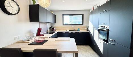 Una cocina moderna con comedor, que incluye una mesa de madera, sillas negras, un reloj negro y una lámpara colgante.