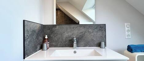 Un baño moderno con tocador blanco, un espejo grande y un protector contra salpicaduras de mármol oscuro.