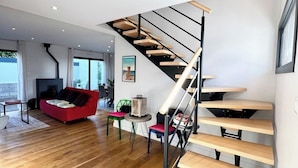 A modern interior with a wooden staircase, a red sofa, and a dining area with chairs.