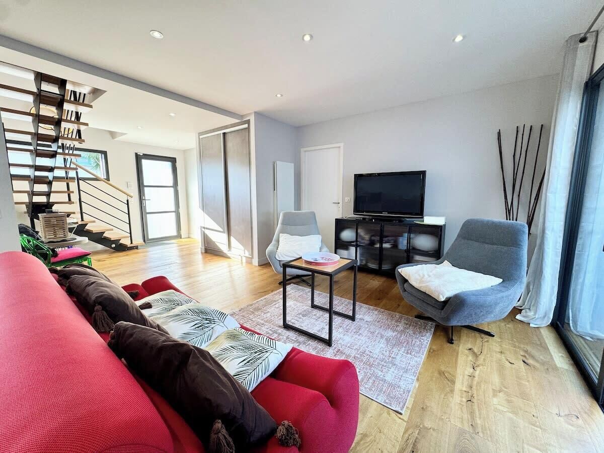 Un salon moderne avec un escalier, un téléviseur à écran plat et une grande fenêtre agrémentée de rideaux.