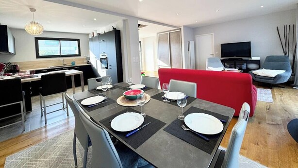 A modern dining area with a rectangular table set for four, a red sofa, and a television in the background.
