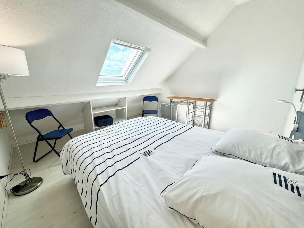 A bedroom with a bed, a desk, a chair, and a skylight.
