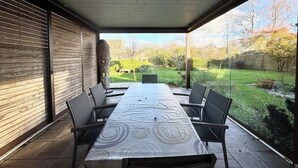 An outdoor dining area with a long table and chairs, a view of a garden, and a wooden wall. - Spacieuse longère archi cosy - Jardin (Quimperlé)