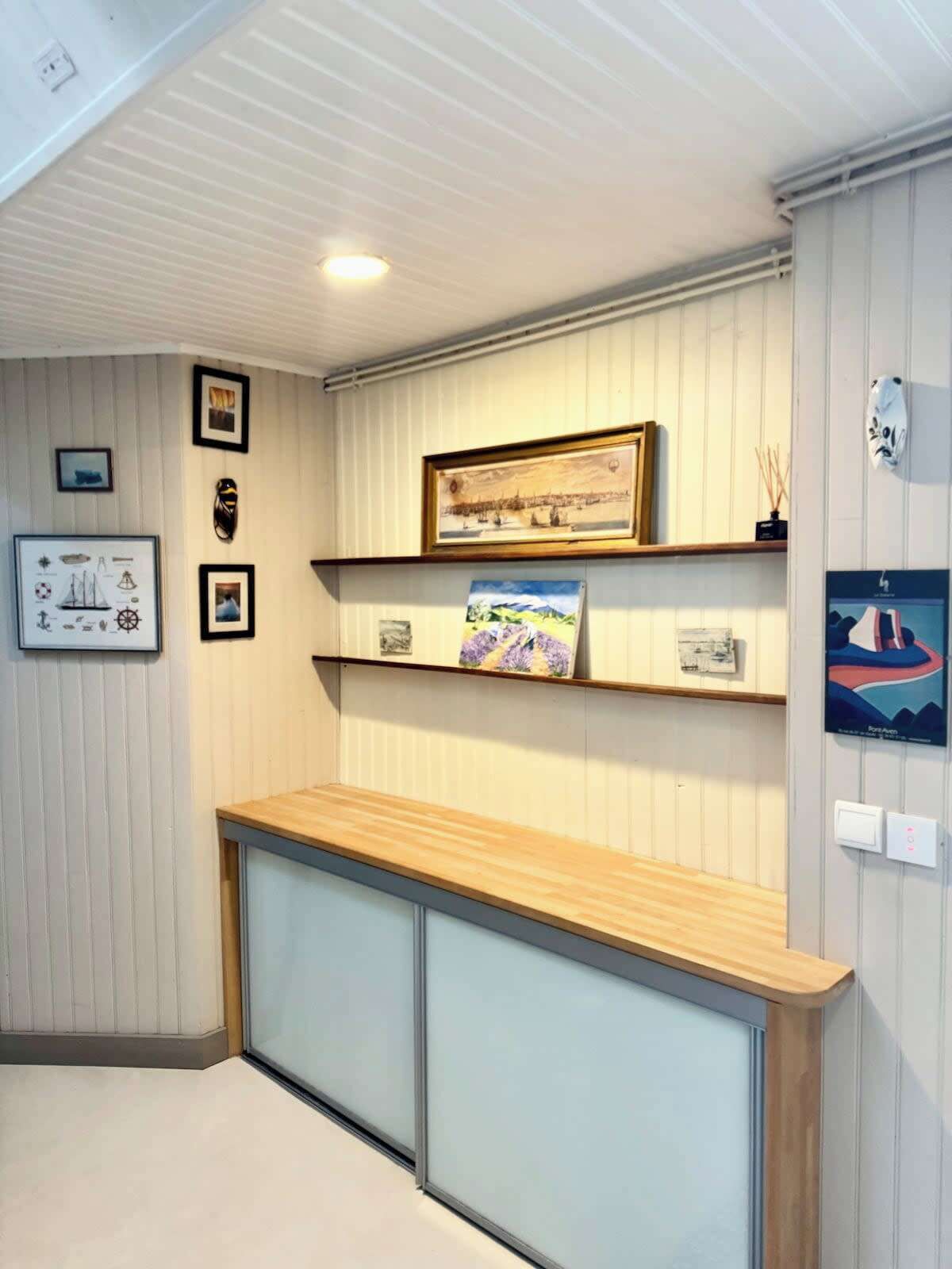 A reception area with a wooden counter, framed nautical and landscape paintings, and a white wall with vertical paneling.