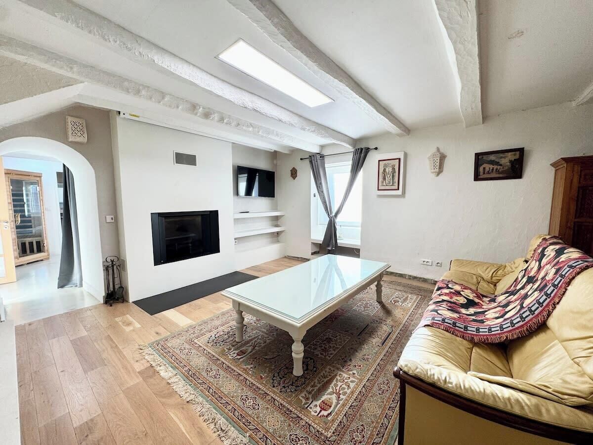 Un salon avec une table basse en verre, un canapé beige, un tapis à motifs, un téléviseur à écran plat et une cheminée.