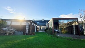A modern house with a well-maintained lawn, a garage, and a patio area. - Spacieuse longère archi cosy - Jardin (Quimperlé)