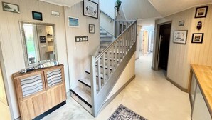 A hallway with a wooden console, a mirror, and a staircase with a metal railing. - Spacieuse longère archi cosy - Jardin (Quimperlé)