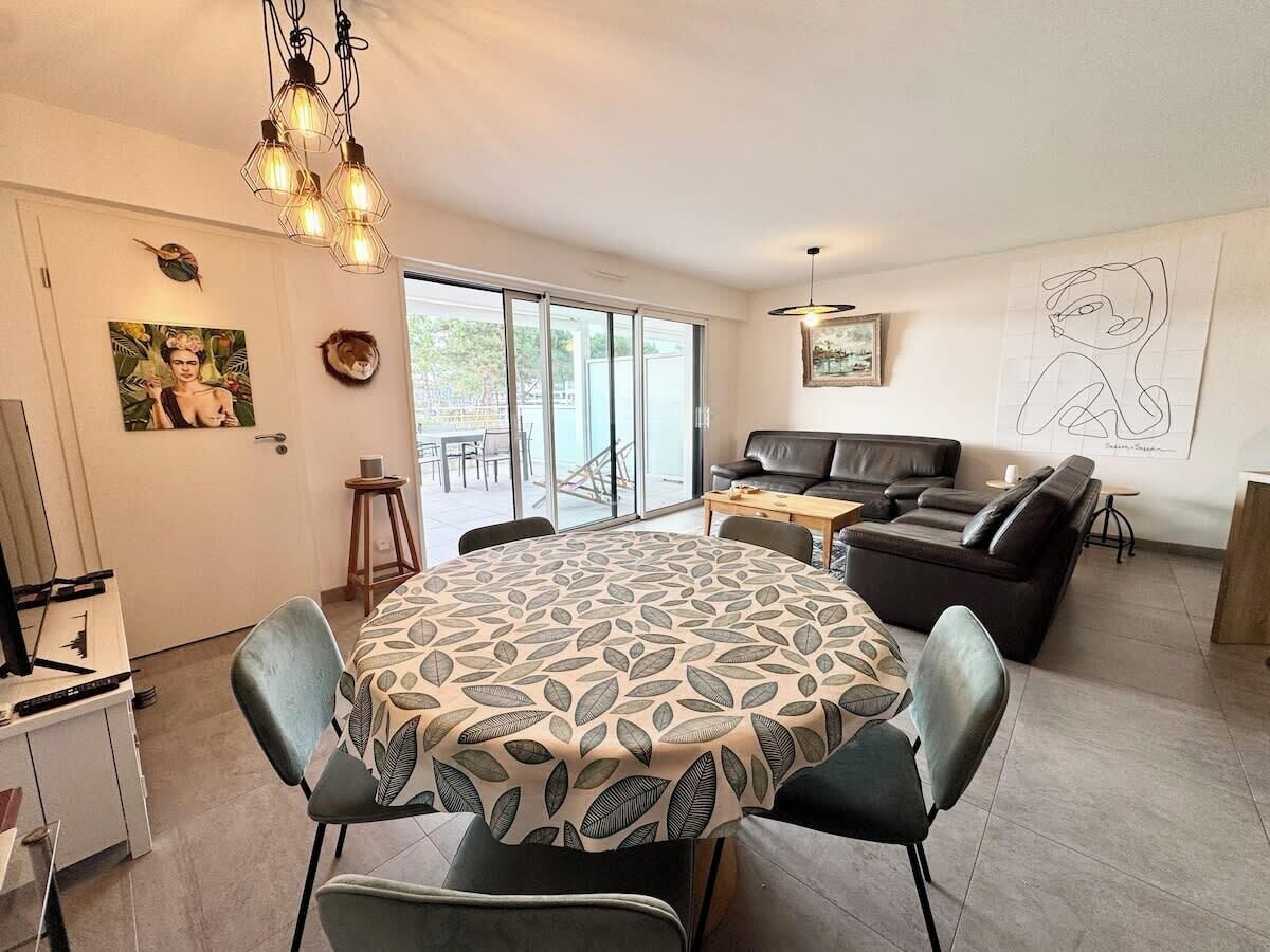 Un salon moderne avec une table de salle à manger ronde, un canapé et une table basse. Une grande fenêtre laisse entrer la lumière naturelle et offre une vue sur l’extérieur.