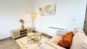 A modern living room with a sofa, a floor lamp, a small table, and a decorative wall piece. - Lovely ! T2 neuf archi cosy 1 (Quimperlé)