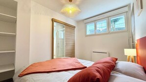 A bedroom with two beds, a window, a radiator, and a ceiling light fixture. - Lovely ! T2 neuf archi cosy 1 (Quimperlé)