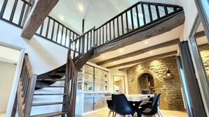 A spacious kitchen with a central island, a dining area with chairs, and a stone fireplace.