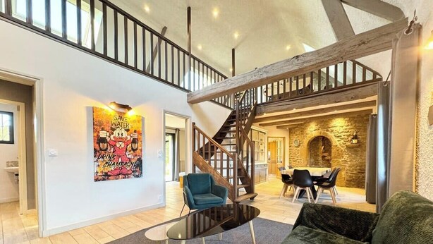 A spacious living area with a staircase leading to a dining area, a fireplace, and a large poster on the wall.