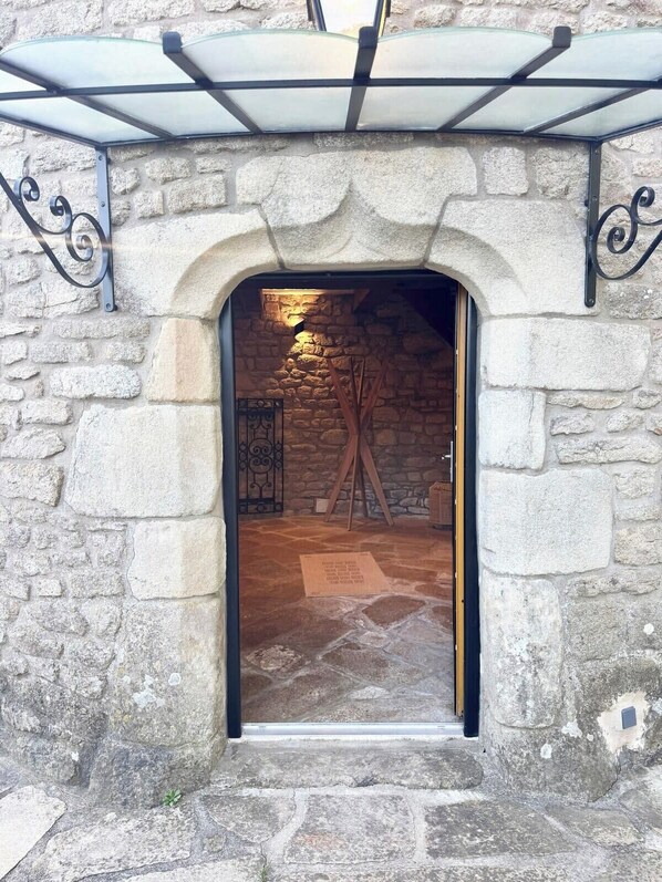 Un arco de piedra que da paso a una habitación con suelo de madera, una escalera y una pequeña mesa con una señal.
