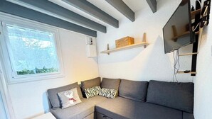 Un salon moderne avec un canapé d’angle gris, une petite table d’appoint blanche et un téléviseur fixé au mur.