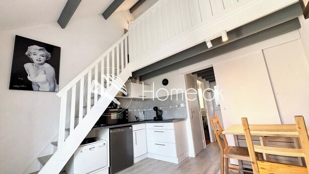 Une cuisine moderne avec des meubles blancs, une table à manger en bois et un escalier menant à l’étage supérieur.