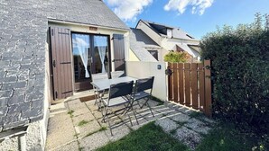 Une terrasse avec une table et des chaises, un portail en bois et une maison avec un toit en pente.