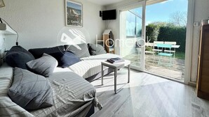 A modern bedroom with a bed, bedside table, and a view of the outdoors through large glass doors. - Maisonnette 300m des plages - Piscine chaufée (Guidel)
