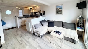 A compact living space with a kitchenette, a sofa bed, a small table, and a television. - Maisonnette 300m des plages - Piscine chaufée (Guidel)