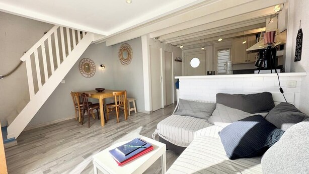 A modern living room with a staircase, a dining area, and a kitchen in the background. - Maisonnette 300m des plages - Piscine chaufée (Guidel)