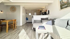 A compact, well-lit room with a bed, a sofa, a dining table, and a small kitchen area. - Maisonnette 300m des plages - Piscine chaufée (Guidel)