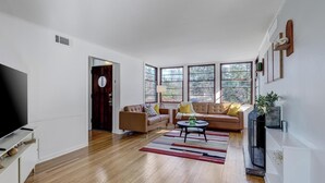 A modern living room with a flat-screen TV, two sofas, a coffee table, and large windows.