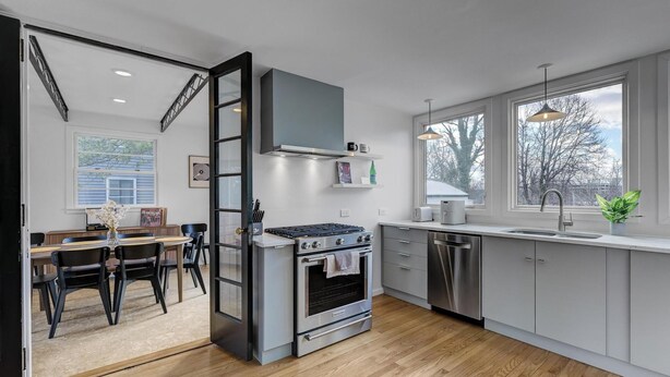 A modern kitchen with stainless steel appliances, a large window, and a dining area with a table and chairs.