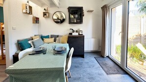 Un comedor con una mesa dispuesta para dos personas, un sofá con cojines, un espejo y vistas al exterior.
