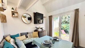 Una sala de estar acogedora con un sofá, una mesa de comedor para dos personas, una cafetera y un televisor montado en la pared.