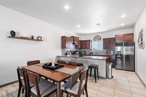 A modern kitchen with wooden cabinets, a stainless steel refrigerator, and a dining area with a table and chairs.