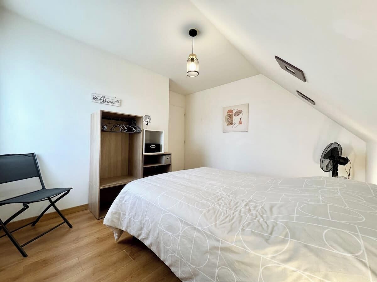 Een slaapkamer met een bed, een bureau, een stoel, een kledingkast, een plafondventilator en een lamp.