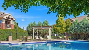 A swimming pool with lounge chairs and a pergola, surrounded by trees and a residential building. - Timberline Retreat – King Bed, Fireplace & Pool! (Fort Collins)
