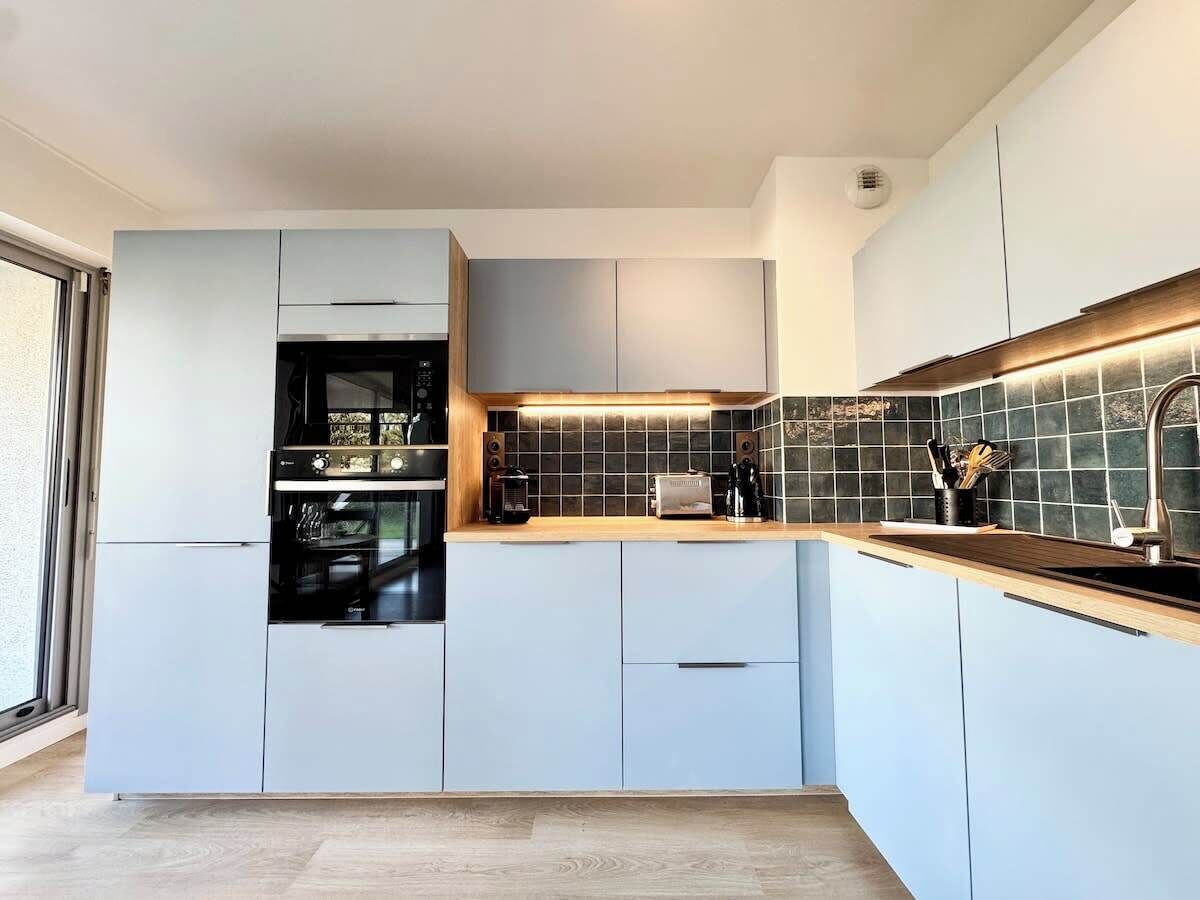 Une cuisine moderne avec des meubles de couleur bleu clair, un plan de travail en bois et un four noir.