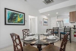 A dining area with a round glass table, four chairs, and a kitchen in the background. - Spacious 2BR Condo w/ Free Parking near Palm Beach (Noord)