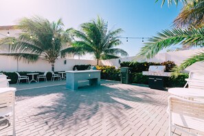 Een terras buiten met een barbecue, zithoek en palmbomen.