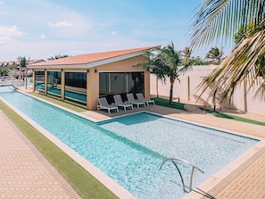 A swimming pool with lounge chairs and a covered area, surrounded by palm trees and a clear sky. - Spacious 2BR Condo with Pool Access in Noord Aruba (Noord)