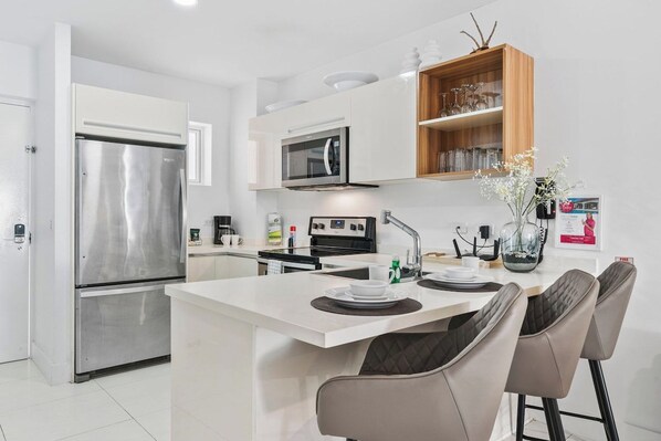 A modern kitchen with a stainless steel refrigerator, microwave, and stove. There is a small island with seating and a coffee machine.