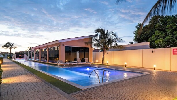 A swimming pool with lounge chairs and a building with large windows. - Poolside Bliss: 2-Bedroom Condo with Patio Noord (Noord)